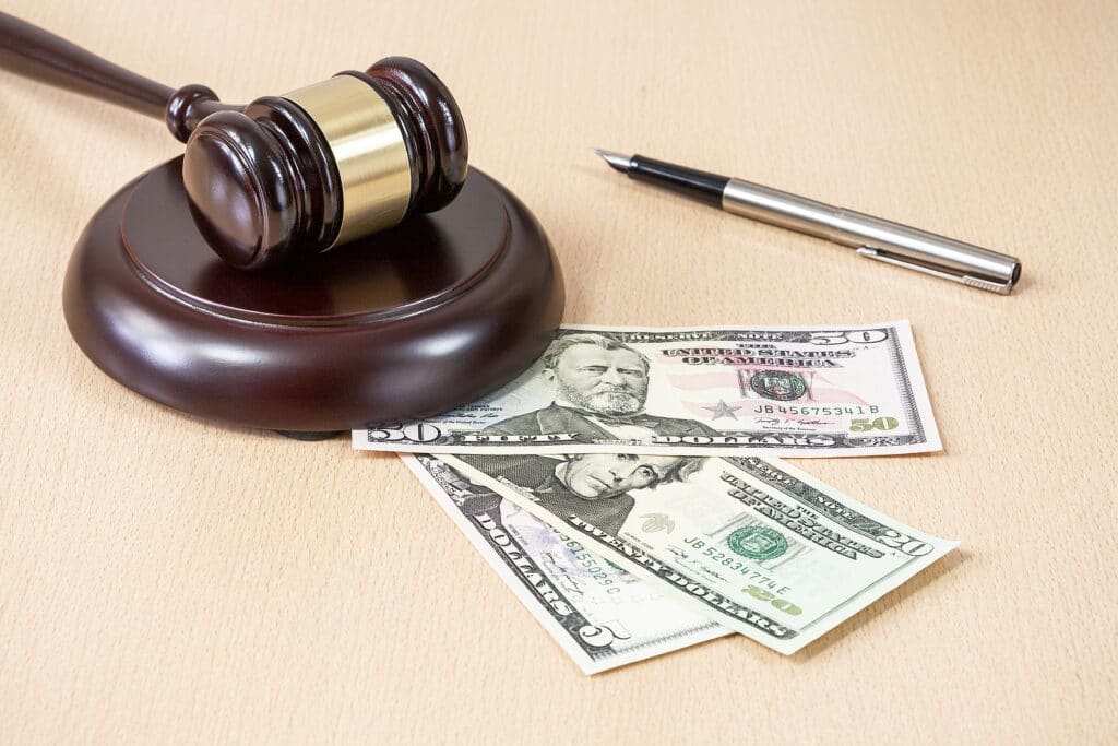 A wooden gavel on wooden table, on brown background, dollars A judge's gavel, a pen, and a $50, $20, and $5 bill laying on a table