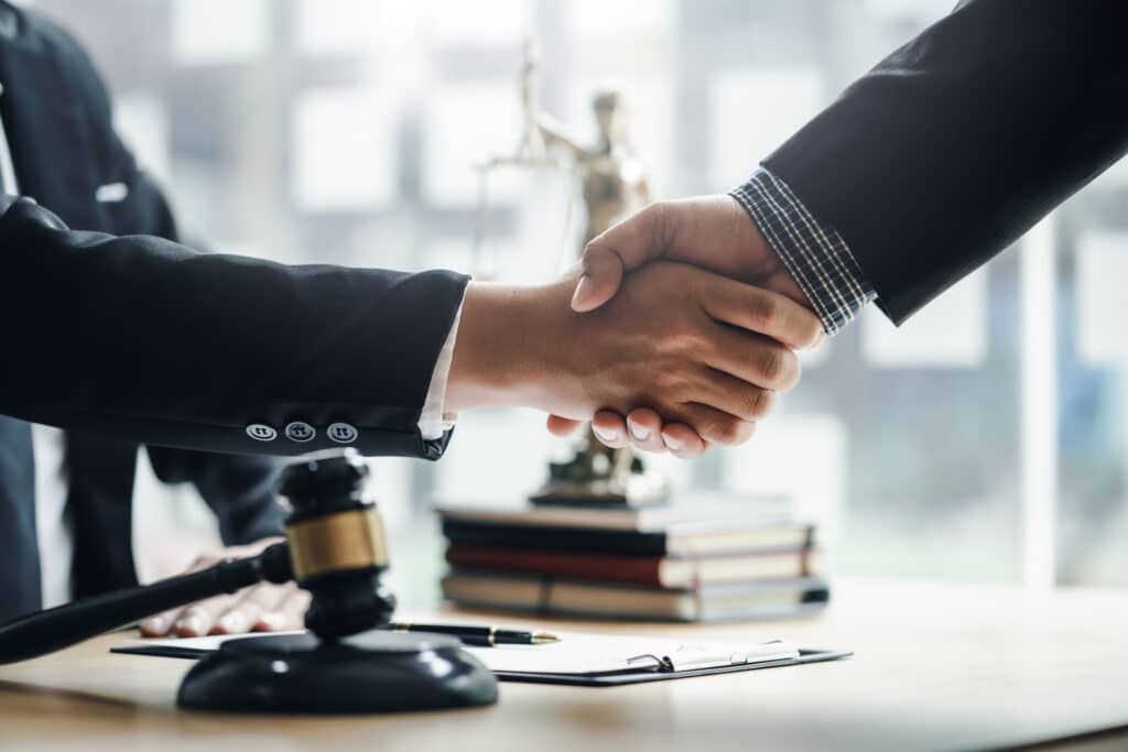 Businessman handshake partner lawyers or attorneys discussing a contract agreement. Business people shaking hands to congratulate success. Two people in suits shaking hands over a judge's gavel