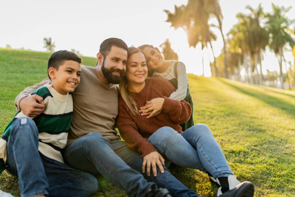 Family sitting on ground in public park A family of four, smiling and sitting down on a hill