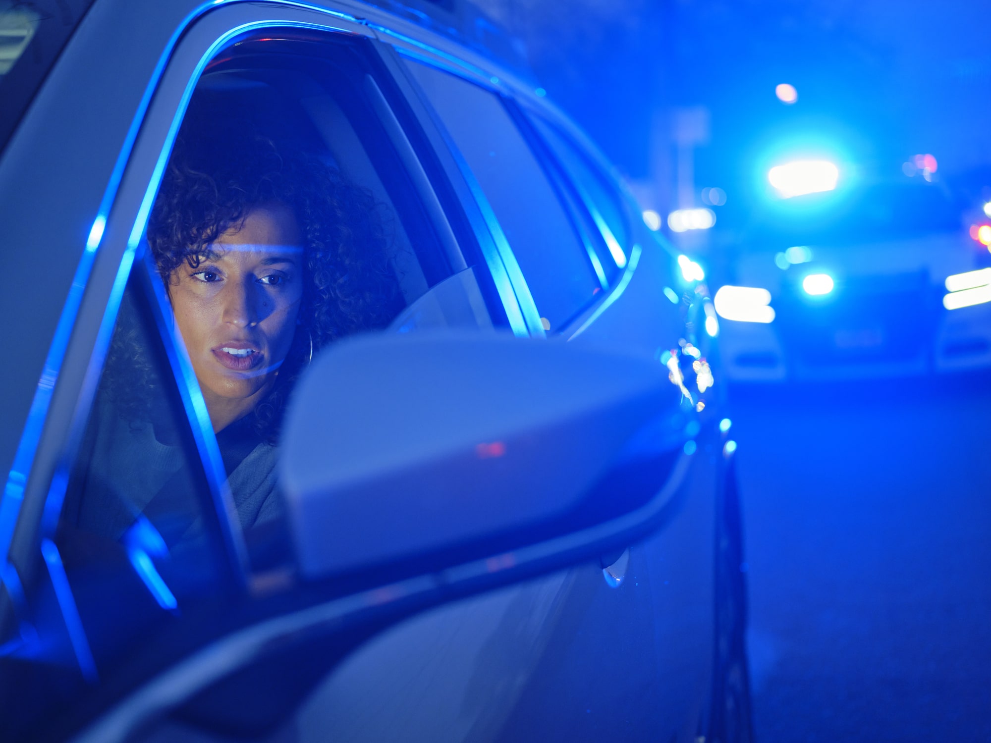 Young Woman Driver Pulled Over By Police at Night Woman behind wheel of car with cop lights flashing behind her
