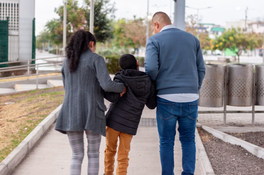 Family walking together, supporting their son with cerebral palsy Two adults walking with a child in the middle